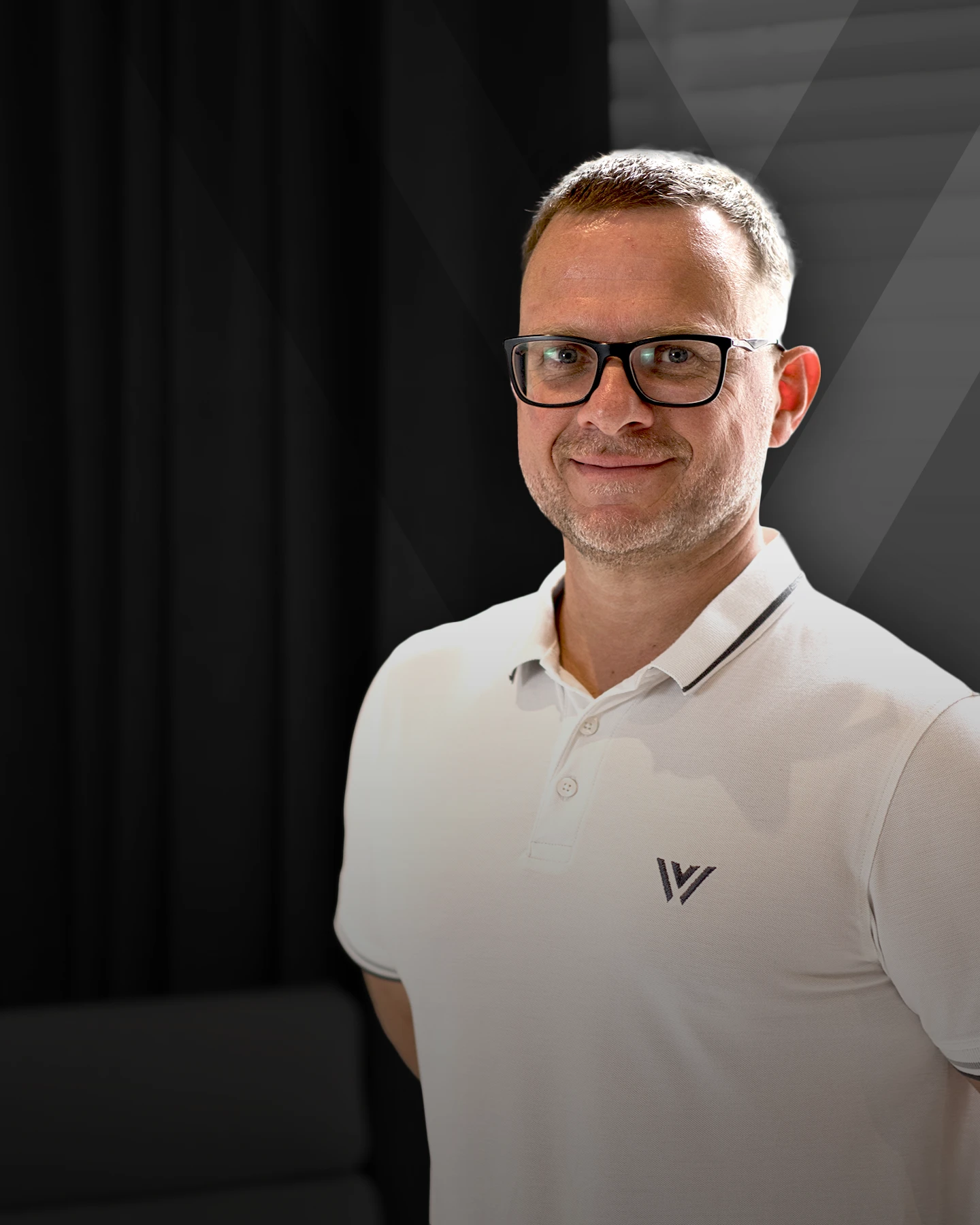 Porträtfoto von Dr. med. Edmund von Werner, Mitarbeiter bei Von Werner, im weißen Poloshirt mit Logo vor dunklem Hintergrund.